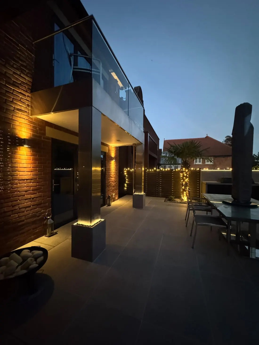 A patio at dusk lit by warm festoon and wall lighting installed by Allview