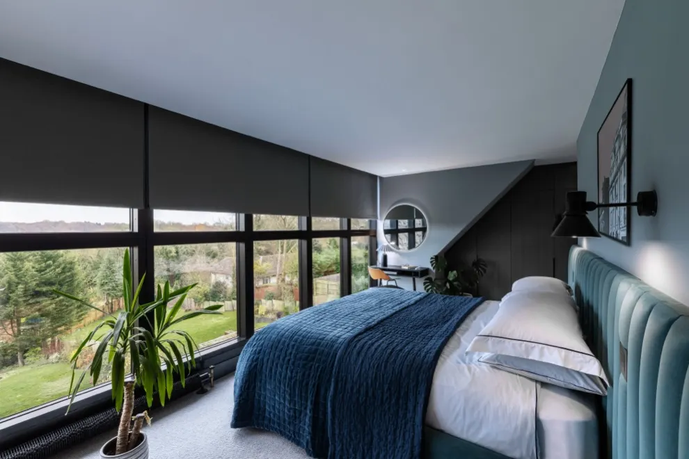 A bedroom with motorised roller blinds lowered across a wall of windows